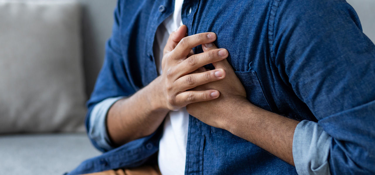 man in denim shirt clutches chest